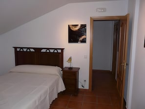 A bedroom with a bed, a nightstand, a wall-mounted lamp, and a door leading to another room.