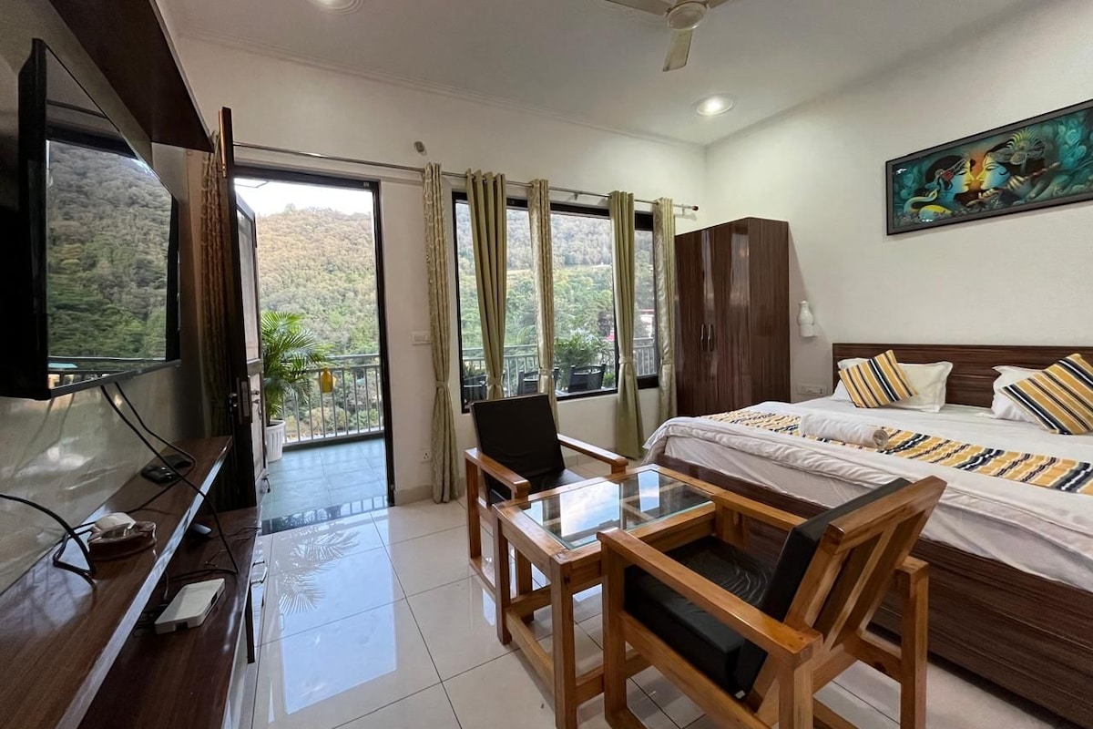 Una camera d'albergo con un letto, una televisione, una scrivania con una sedia, un balcone con tende e un quadro appeso al muro.