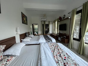 Una camera d'albergo con due letti, televisione, ventilatore a soffitto e una finestra con tende.