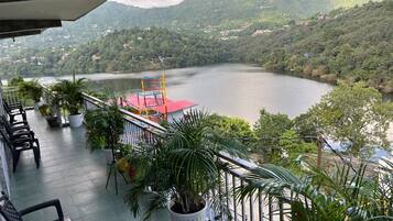 Un balcon orné de plantes en pot, un toit rouge et une vue sur un lac entouré de collines.