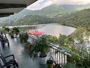 Un balcón con plantas en macetas, techo rojo y vista a un lago rodeado de colinas.