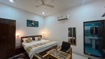 A bedroom with a bed, bedside table, wardrobe, ceiling fan, wall-mounted air conditioner, and a view of the bathroom.
