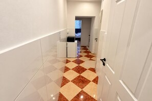 A narrow hallway with a checkered floor, white walls, and a door at the end. - Your Vienna Reunion 2BR and Lounge for 6 (Vienna)