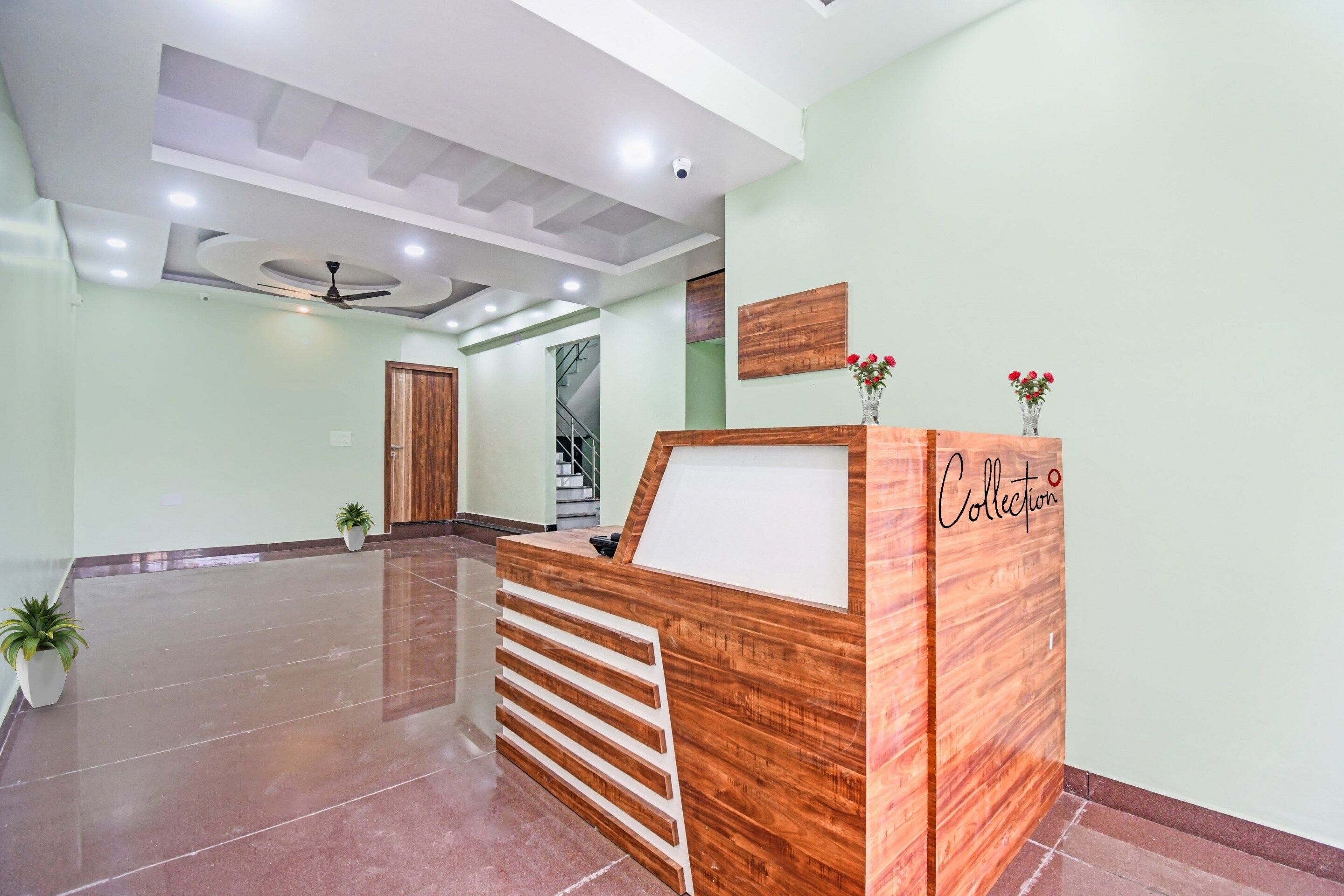 A reception desk with a wooden finish, a ceiling fan, and a staircase in the background.