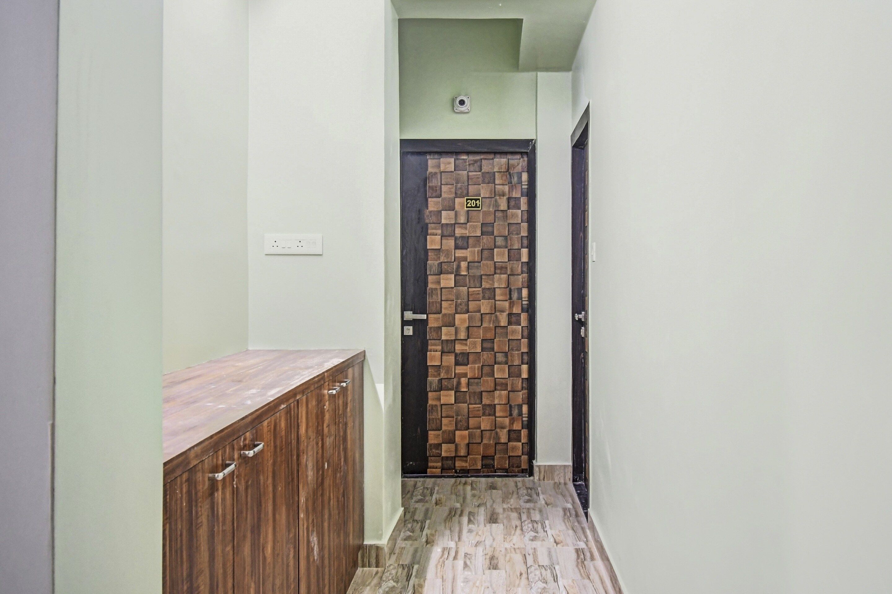 Um corredor com um armário de madeira, uma porta revestida de azulejos e um interruptor de luz na parede.