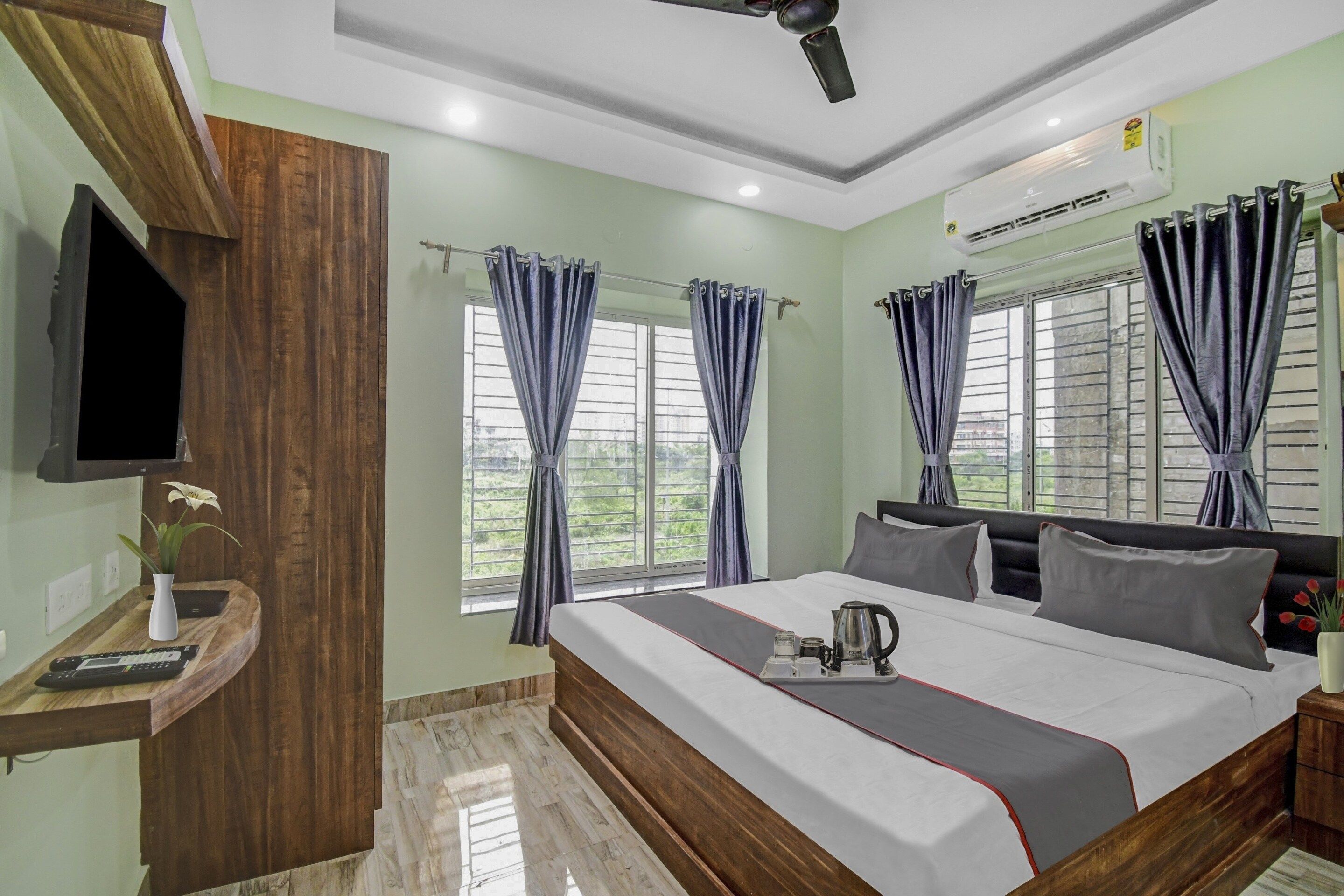 A hotel room with a bed, a TV mounted on the wall, a desk with a remote control, and a window with curtains.