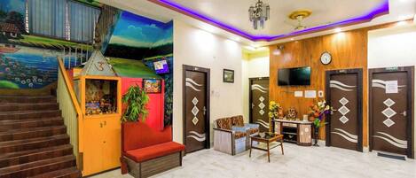 A hotel lobby with a staircase, a reception desk, a TV, and a clock.