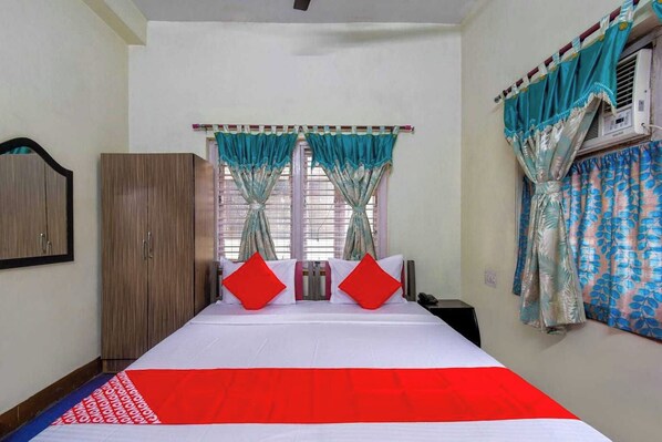 A bedroom with a bed, curtains, a wardrobe, and a window with an air conditioning unit.