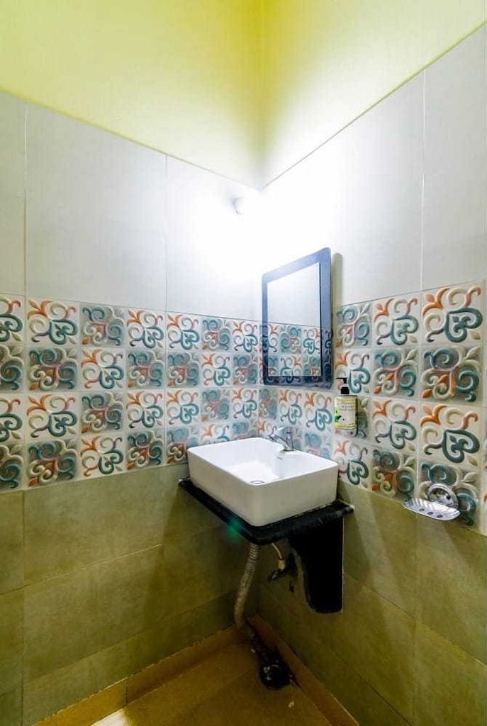 Un baño con un lavamanos blanco, un espejo y azulejos estampados en las paredes.