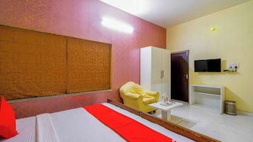 Una habitación de hotel con una cama, un sillón amarillo, un televisor y un armario.