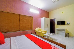 A hotel room with a bed, a yellow armchair, a TV, and a wardrobe.