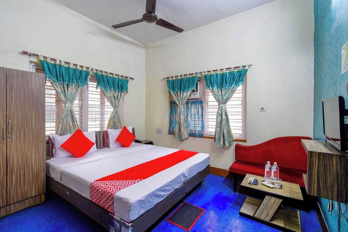 A hotel room with a bed, a red sofa, a TV, and curtains.