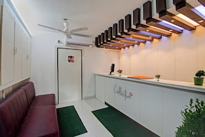 A reception area with a white reception desk, a ceiling fan, and a modern light fixture. - Collection O Green Leaf Near Acropolis (Kolkata)