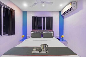 A hotel room with a bed, a bedside table with a telephone, a nightstand with a vase of flowers, and an air conditioning unit on the wall. - Collection O Green Leaf Near Acropolis (Kolkata)