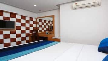 Habitación de hotel con pared a cuadros, un televisor de pantalla plana sobre un escritorio y una cama con colcha a rayas azul y blanca, además de un equipo de aire acondicionado en la pared.
