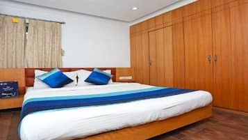Hotellihuone, jossa on suuri sänky, puinen vaatekaappi ja yöpöytä.