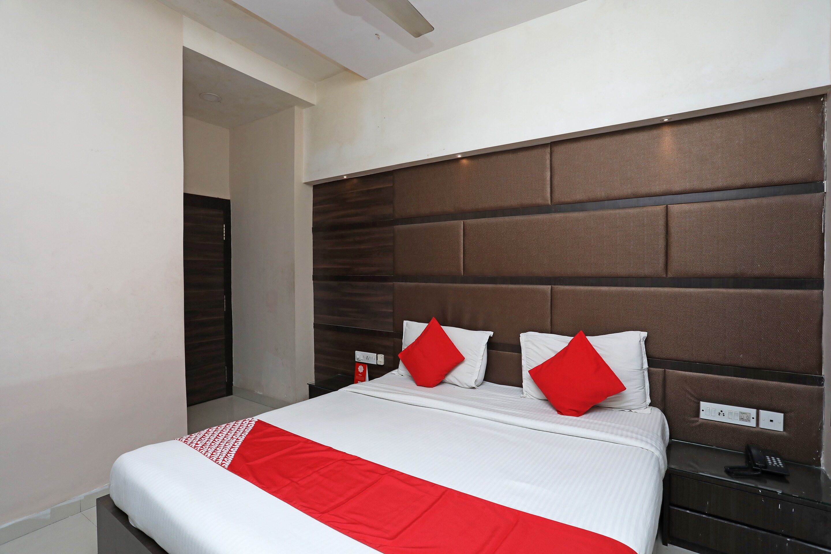 A modern hotel room with a large bed, a wooden headboard, and a red and white bedspread.