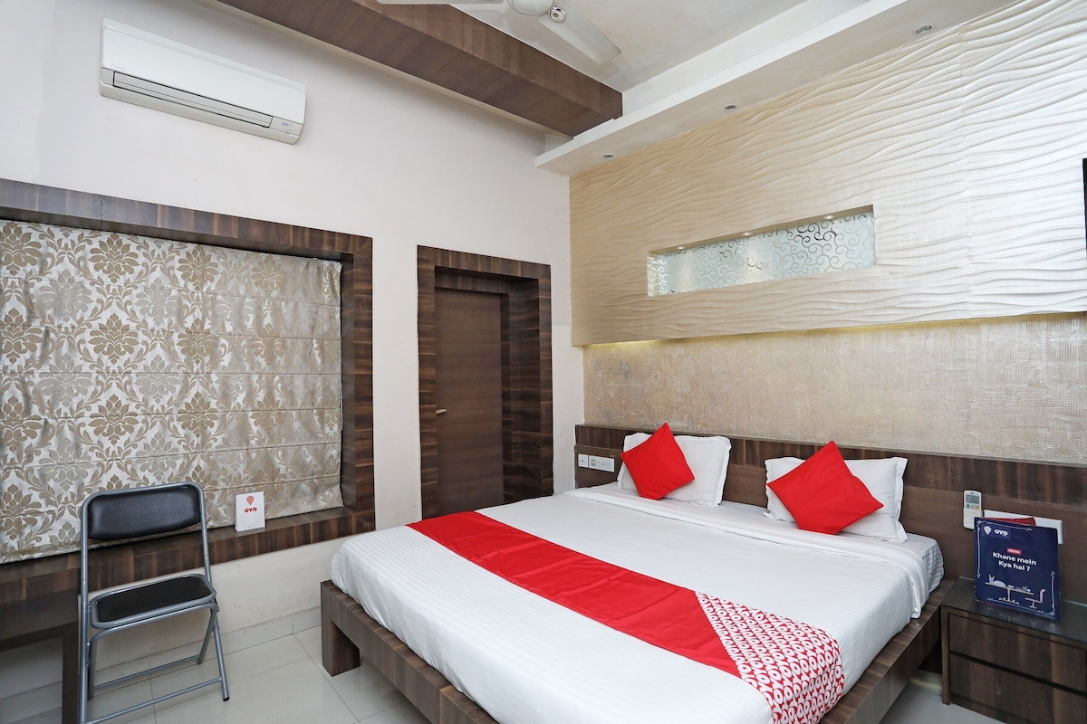 A hotel room with a bed, a desk, a chair, and a wall-mounted air conditioner.