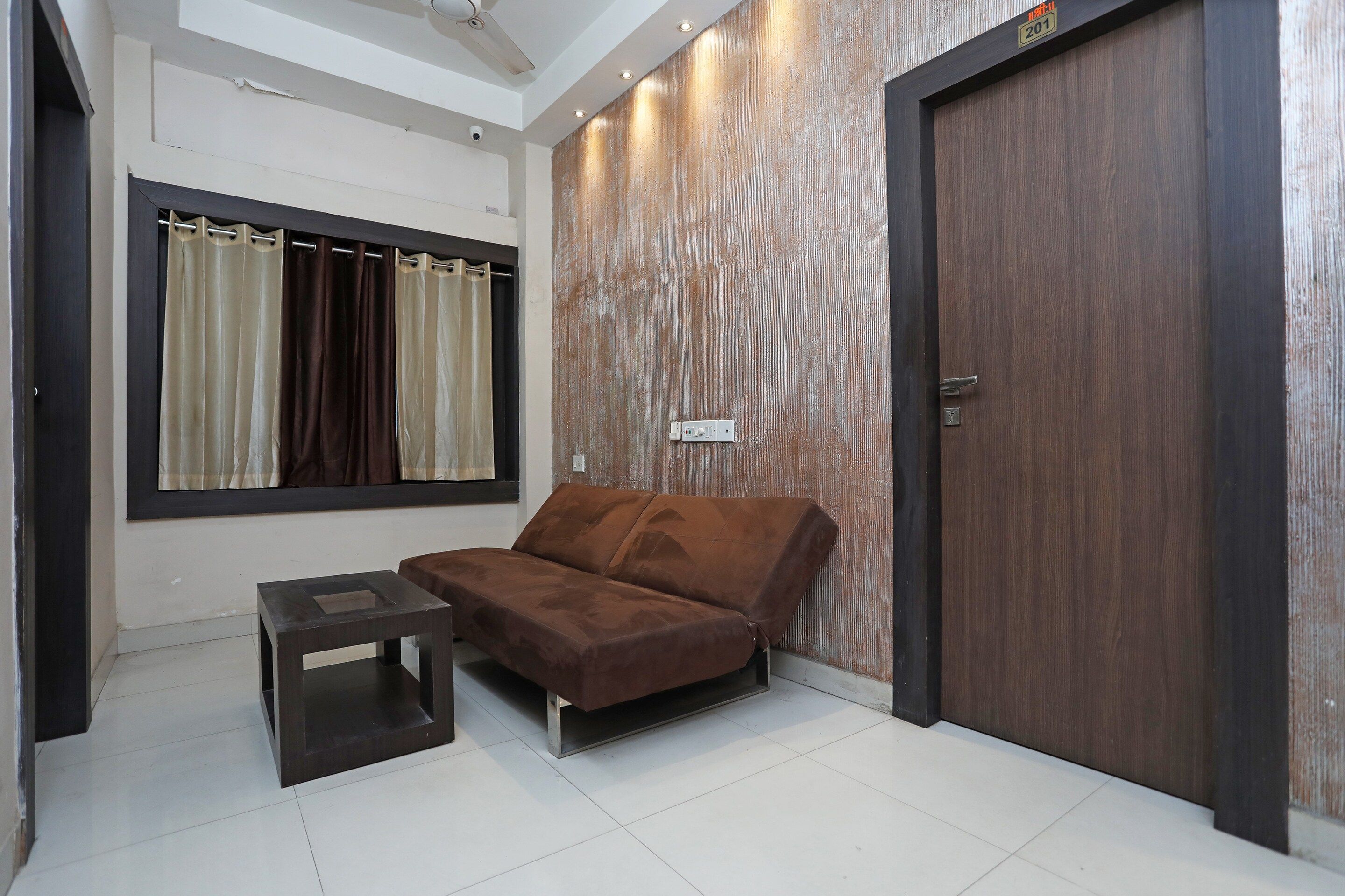 A room with a brown sofa, a small table, a window with curtains, and a wooden door.