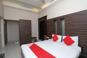 A hotel room with a large bed, a wardrobe, a small stool, and a nightstand. - Hotel O South Fern (Kolkata)