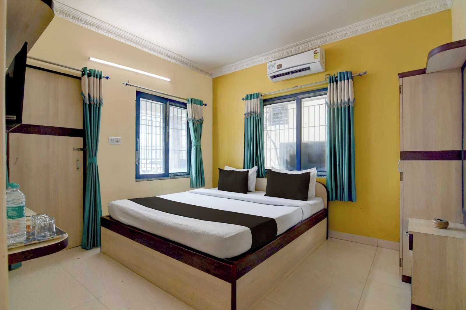 A hotel room with a bed, curtains, an air conditioning unit, and a window.