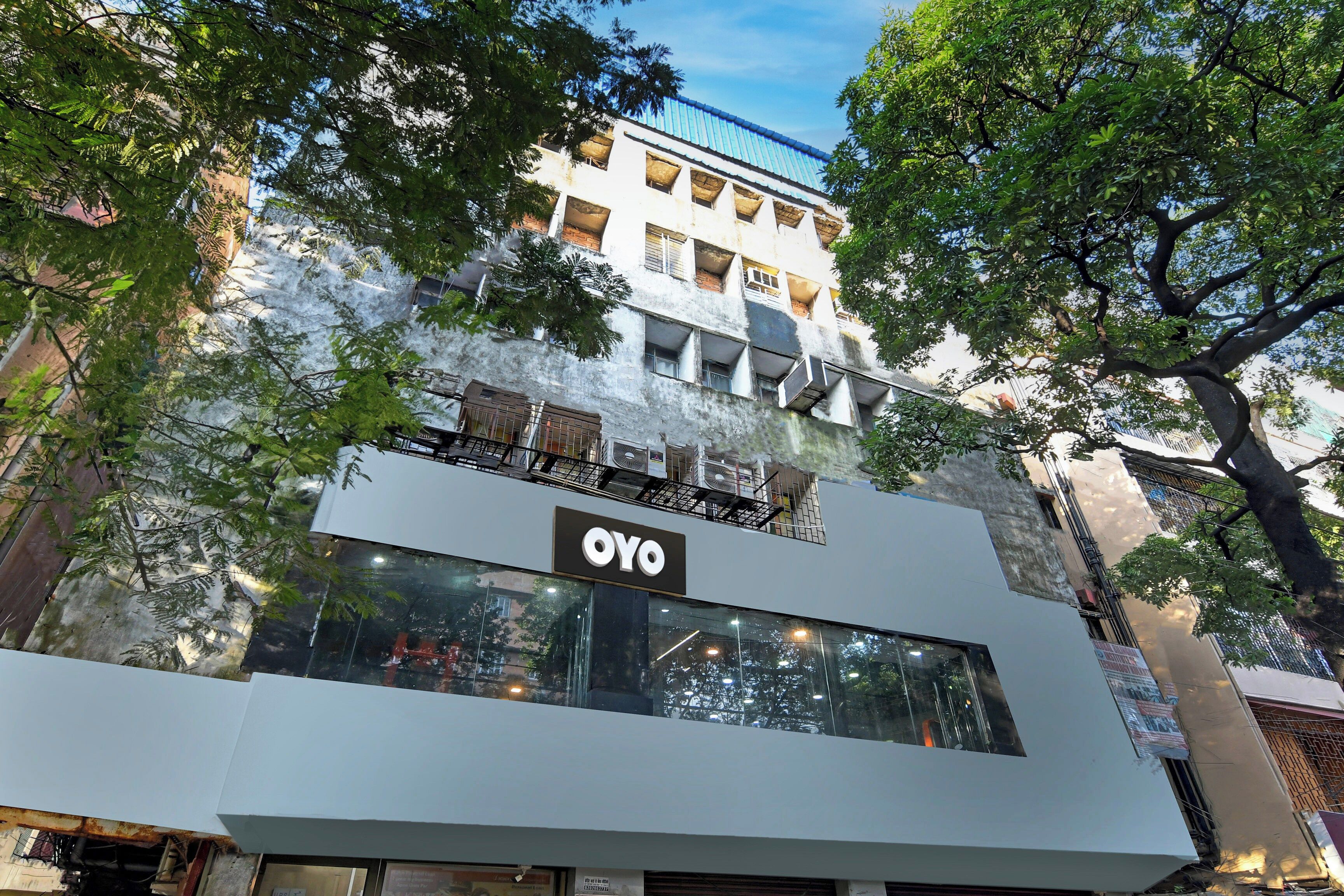 Un edificio moderno con un llamativo letrero de OYO, amplios ventanales y un balcón con barandilla.