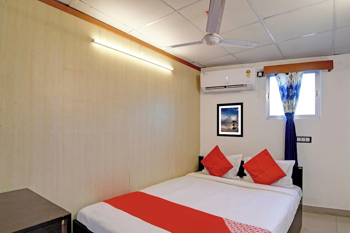 A hotel room with a bed, a ceiling fan, an air conditioning unit, a window with curtains, and a wall-mounted picture.
