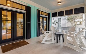 A porch with white rocking chairs and a table, a teal door, and a white railing. - WaterColor | 2 King Suites, Beach & Pools (Santa Rosa Beach)