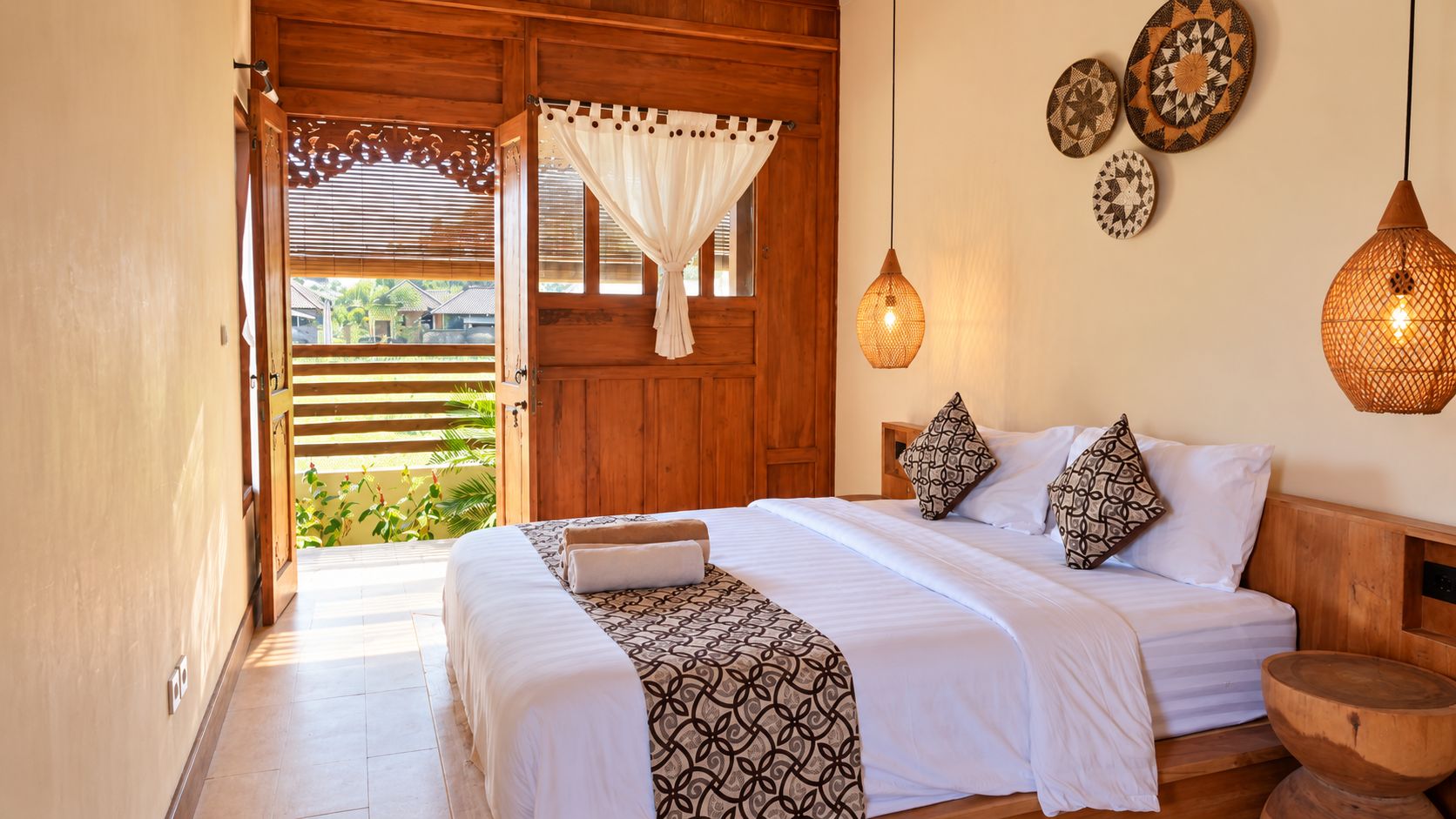 Quarto com porta de madeira, cama com roupa de cama estampada e objetos decorativos nas paredes.