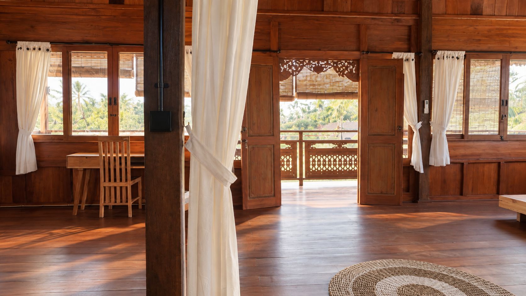 Um quarto de madeira com mesa e cadeiras, um banco e vista através de uma porta de madeira.