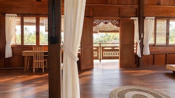 Um quarto de madeira com mesa e cadeiras, um banco e vista através de uma porta de madeira.