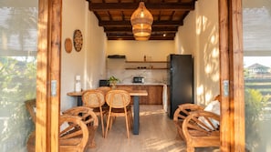 Cozinha com área de refeições, cadeiras de madeira, luminária pendente e geladeira.