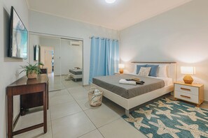 A hotel room with a bed, bedside tables, a desk, a mirror, and a blue curtain. - Experience this stylish 3BR/2BA Gold Coast condo togheter with your family. Relax on your private covered patio with gas BBQ, or enjoy resort pools, tennis courts and a gym in this gated community. Aruba’s beautiful beaches are just minutes away. (Noord)
