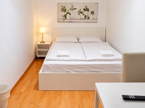 A hotel room with a bed, a nightstand, a lamp, a painting, and a table with a remote control. - The Vienna Get Together 3BR for 8 near Westbahnhof (Vienna)