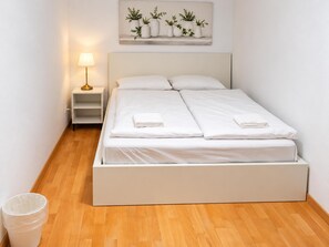 A double bed with white bedding, a bedside table with a lamp, and a wall-mounted plant shelf. - The Vienna Get Together 3BR for 8 near Westbahnhof (Vienna)