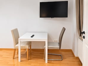 A modern room with a white table, two chairs, a TV on the wall, and a door with curtains. - The Vienna Get Together 3BR for 8 near Westbahnhof (Vienna)
