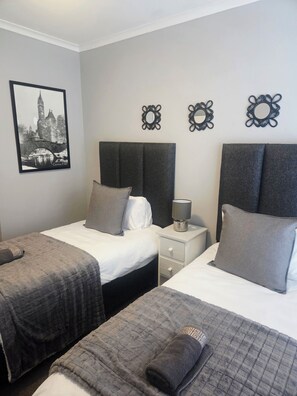 A hotel room with two beds, a nightstand with a lamp, decorative wall mirrors, and a framed cityscape picture. - Serene 2-bedroom apartment in Bloubergstrand perfect for your getaway (Cape Town)