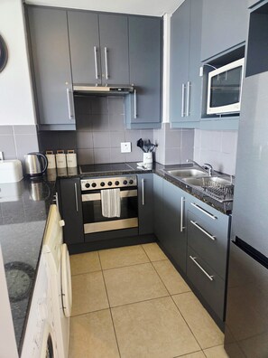 A compact kitchen with grey cabinets, a stainless steel stove, a microwave, and a built-in oven. - Serene 2-bedroom apartment in Bloubergstrand perfect for your getaway (Cape Town)