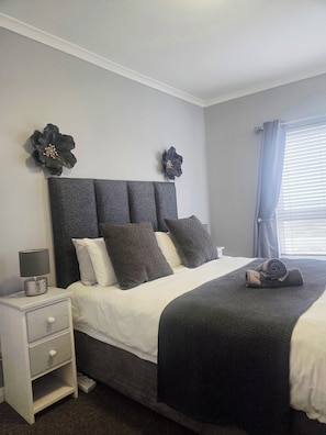 A bedroom with a bed, nightstand, and decorative wall flowers. - Serene 2-bedroom apartment in Bloubergstrand perfect for your getaway (Cape Town)