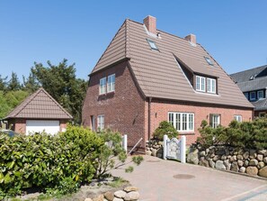Ein zweigeschossiges Backsteinhaus mit geneigtem Dach, einer Garage und einem gepflegten Garten mit Sträuchern und einer Steinmauer.
