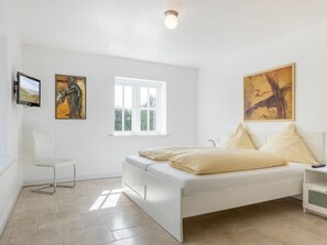 Ein Schlafzimmer mit einem Bett, einem Sessel, einem Fenster und zwei Bildern an der Wand.