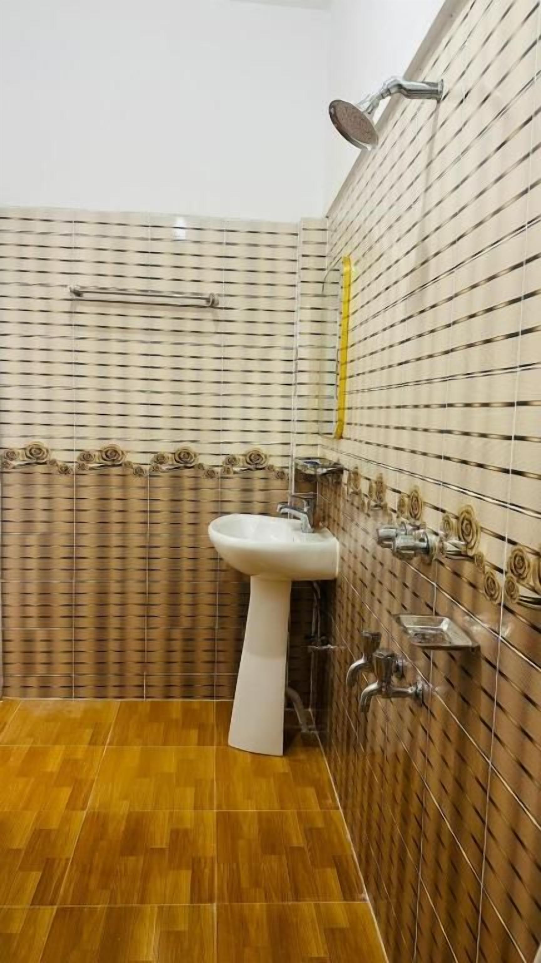 Un baño con un lavabo blanco de pedestal, una ducha y baldosas con diseño en las paredes y el suelo.