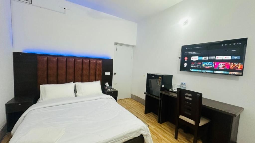 A hotel room with a bed, a desk, a chair, a television, and a wall-mounted screen displaying a streaming service interface.