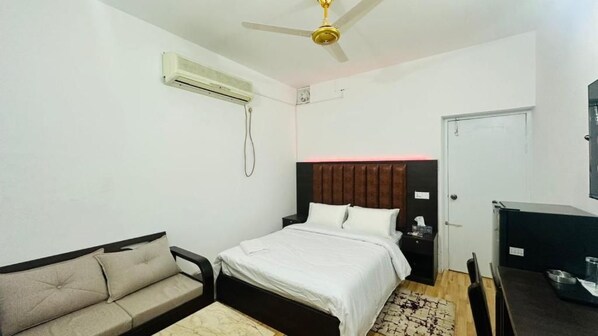 A bedroom with a bed, a sofa, a desk, a chair, an air conditioning unit, and a ceiling fan.