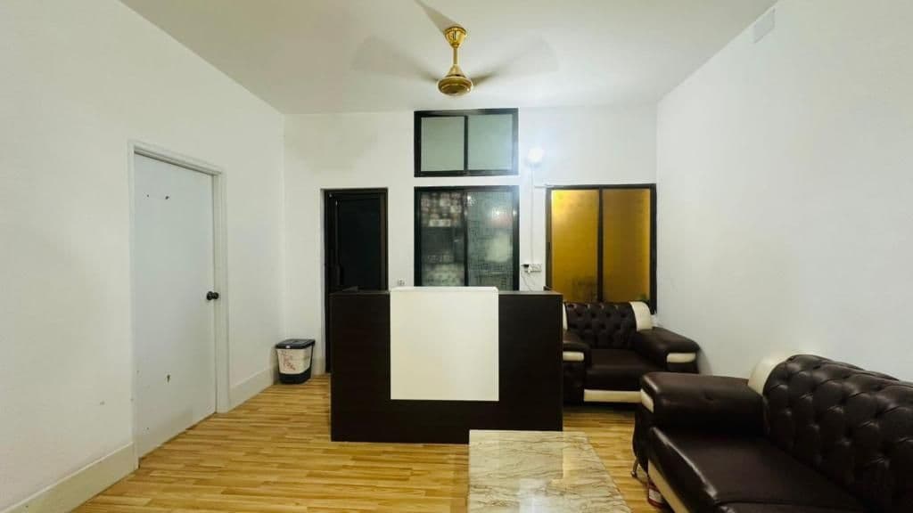 A room with a wooden floor, a black sofa, a white reception desk, and a ceiling fan.