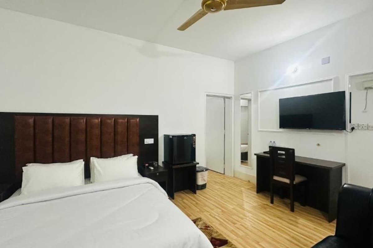 Una camera d'albergo con un letto, una scrivania, una sedia, una televisione e una ventola a soffitto.