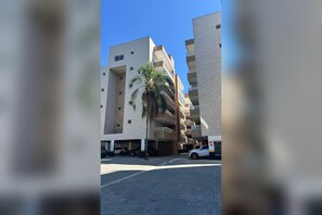 A multi-story building with a parking garage and a palm tree in front. - New Listing (Ubatuba)