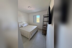 A bedroom with a bed, a window, and a black shelf unit. - New Listing (Ubatuba)
