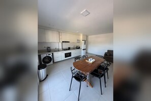 A modern kitchen with white cabinetry, a wooden dining table, and a built-in washing machine. - New Listing (Ubatuba)