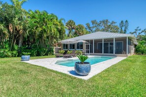 Ein modernes Haus mit Swimmingpool, umgeben von üppiger Vegetation und Palmen.
